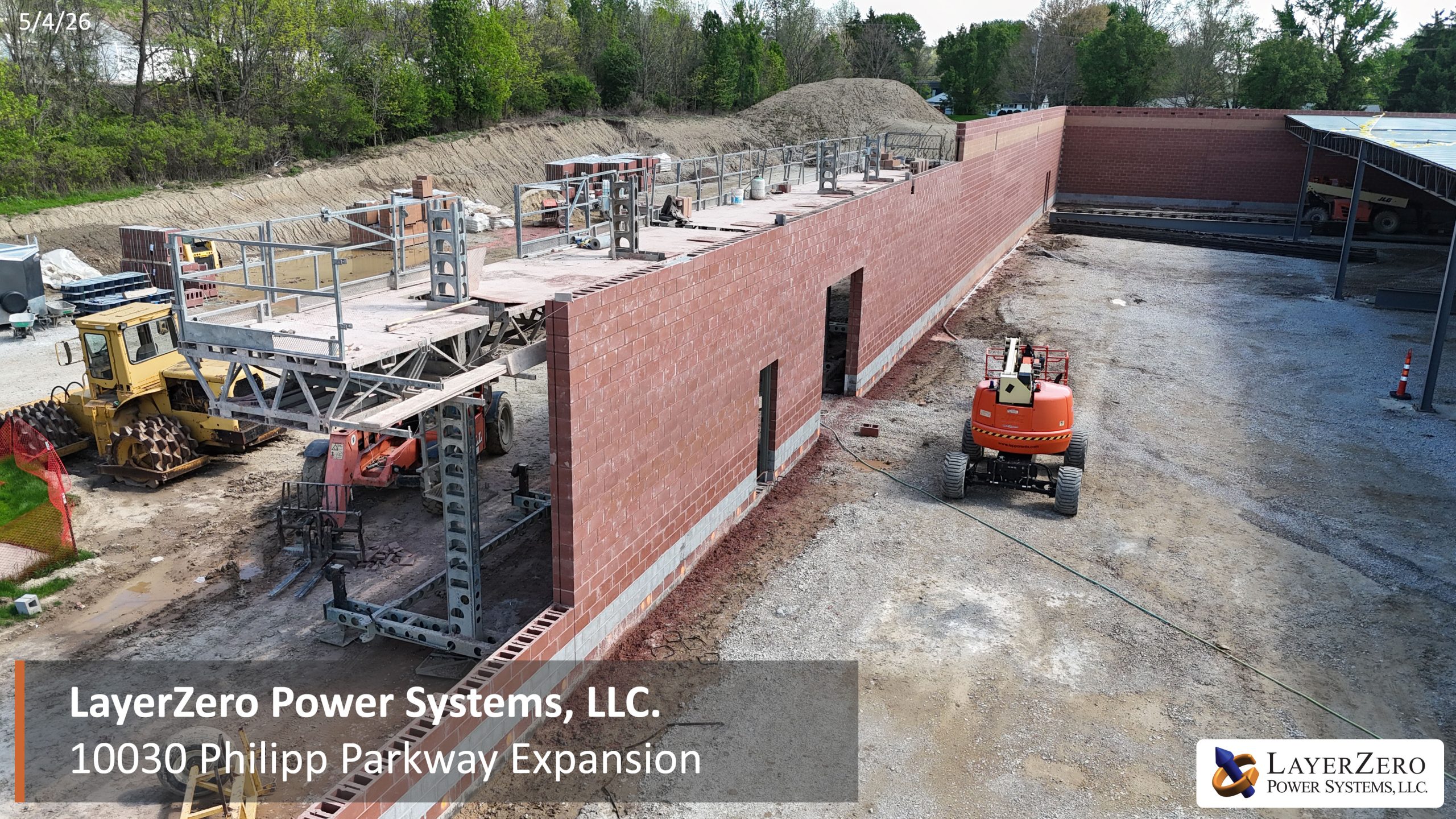 Aerial view of The LayerZero Expansion showing exterior masonry walls, roofing installation, construction equipment, and active site development in progress.