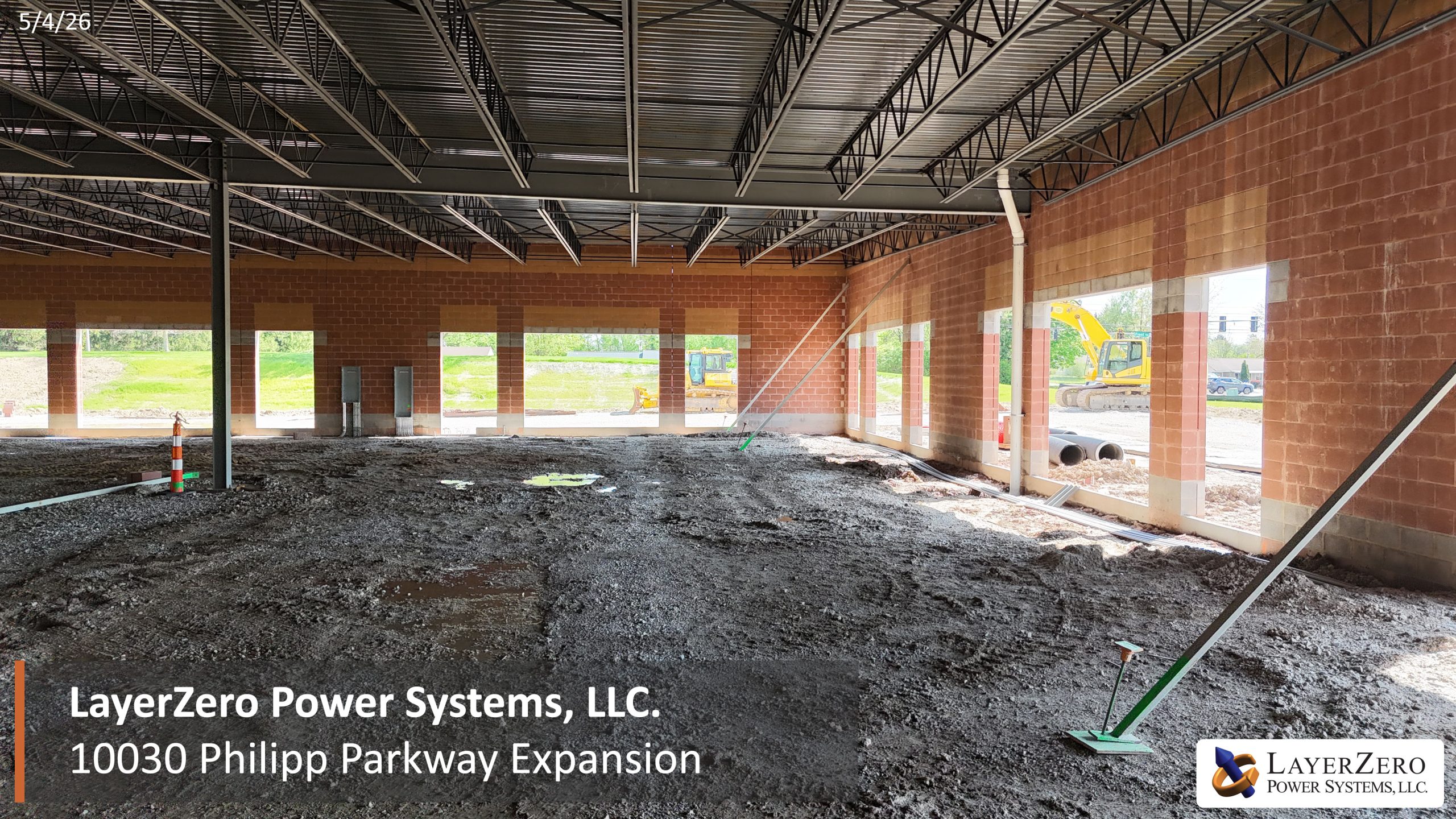 Interior view of The LayerZero Expansion showing structural steel framing, masonry walls, open manufacturing space, and ongoing construction activity.
