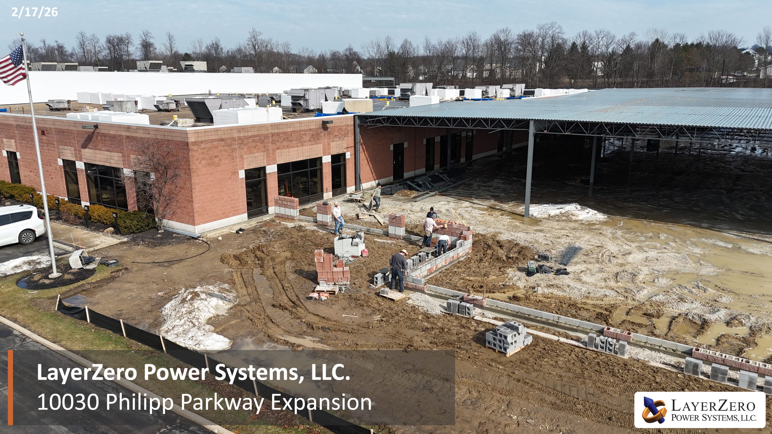 Construction crews installing masonry walls at LayerZero Power Systems, LLC expansion with covered steel canopy attached to existing building