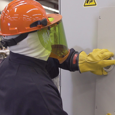 LayerZero Power Systems technician wearing arc-flash PPE operating electrical equipment in manufacturing facility
